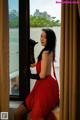 A woman in a red dress and black gloves leaning against a window.