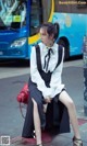 A woman sitting on a fire hydrant in front of a bus.