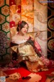 A woman in a kimono sitting on a red carpet holding a fan.