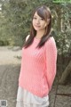 A woman wearing a pink sweater standing in front of a tree.