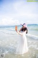 A woman in a white dress and a pink hat standing in the ocean.