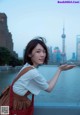 A woman standing in front of a body of water holding a red bag.